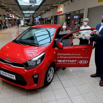 Björn-Alexander Sommer (Leiter Verkauf KIA Bremen, Werner Automobile GmbH) gratuliert und übergibt den symbolischen Schlüssel für das neue Gefährt. Glückwünsche und Blumen gibt es auch von Jolanta Butenaite (Senior Center Manager, Walle-Center), Foto: Martin Rospek.